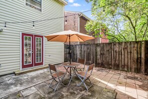 A patio with a table and chairs, a wooden fence, and a house with a red door. - LALALAND -2 master suites, king bed,  comfort & location “No chores” at checkout (Lafayette)