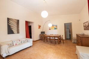 A living room with a sofa, dining table, chairs, a TV, artwork, and a lamp.