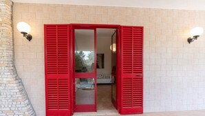 Une porte avec des volets rouges, un mur de pierre et deux lampes fixées au mur.