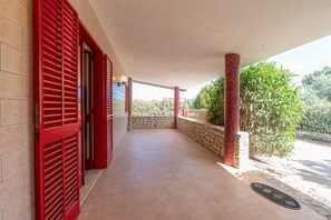 A covered outdoor area with red shutters, a stone wall, and a tiled floor.