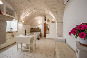 Una habitación acogedora con techo de piedra, una cama, zona de comedor con mesa y sillas, y una pequeña kitchenette.