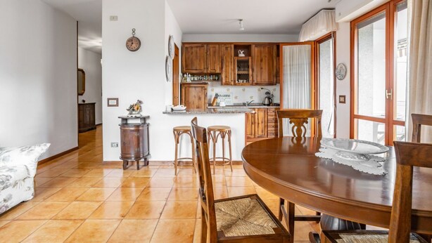 A dining area with a wooden table and chairs, a kitchen with wooden cabinets, and a white wall clock. - GuestHost - Spacious and bright 130 sqm apartment, perfect for 4 people, located on the second floor of a building WITHOUT a lift (stairs to access it).The apartment is located 4.1 km from the center of Lucca: in just 13 minutes by bus you can reach the  (Lucca)