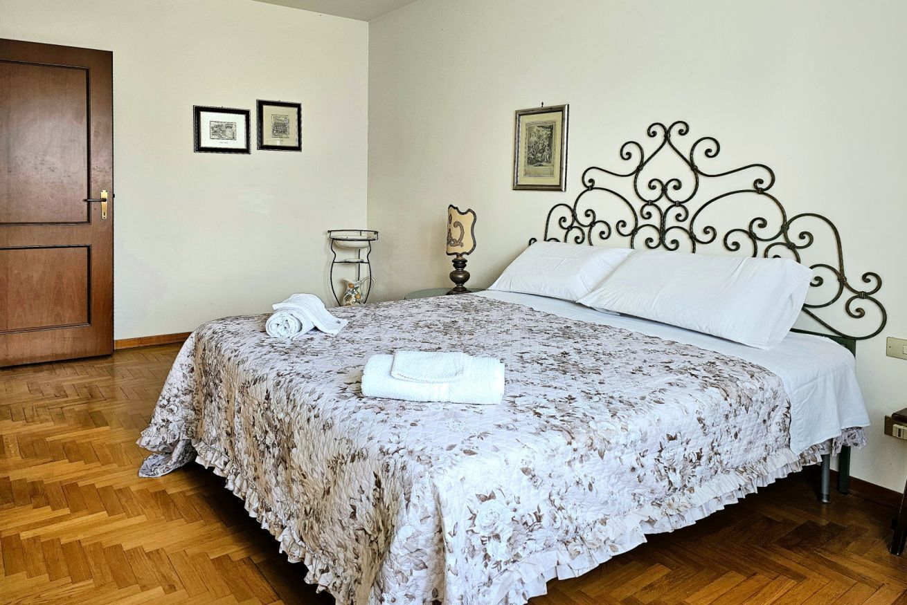 A bedroom with a bed, a wooden door, a bedside table with a lamp, and a framed picture on the wall.