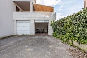 A residential building with a garage, a balcony, and a hedge.
