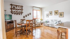 A living room with a dining area, a TV, and a wall-mounted shelf with kitchen utensils. - GuestHost - Spacious and bright 130 sqm apartment, perfect for 4 people, located on the second floor of a building WITHOUT a lift (stairs to access it).The apartment is located 4.1 km from the center of Lucca: in just 13 minutes by bus you can reach the  (Lucca)