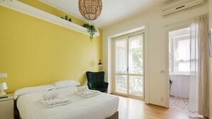 Een slaapkamer met een bed, nachtkastje, lamp, stoel en een openslaande deur naar een balkon.
