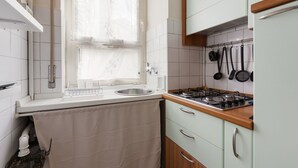 Een keuken met raam, spoelbak, fornuis en hangende keukengerei.