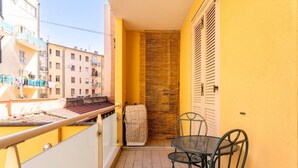 A balcony with a table and chairs, a radiator, a towel, and a window overlooking a building.