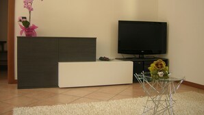 Una sala de estar moderna con un televisor de pantalla plana, un sofá blanco, una mesa de centro de vidrio y una planta de orquídea decorativa.