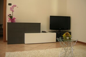 Una sala de estar moderna con un televisor de pantalla plana, un sofá blanco, una mesa de centro de vidrio y una planta de orquídea decorativa.