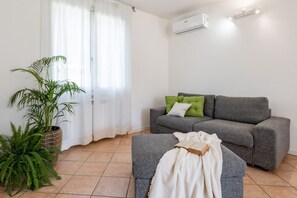 Una sala de estar con un sofá gris, un cojín verde, una manta blanca y una planta en maceta.