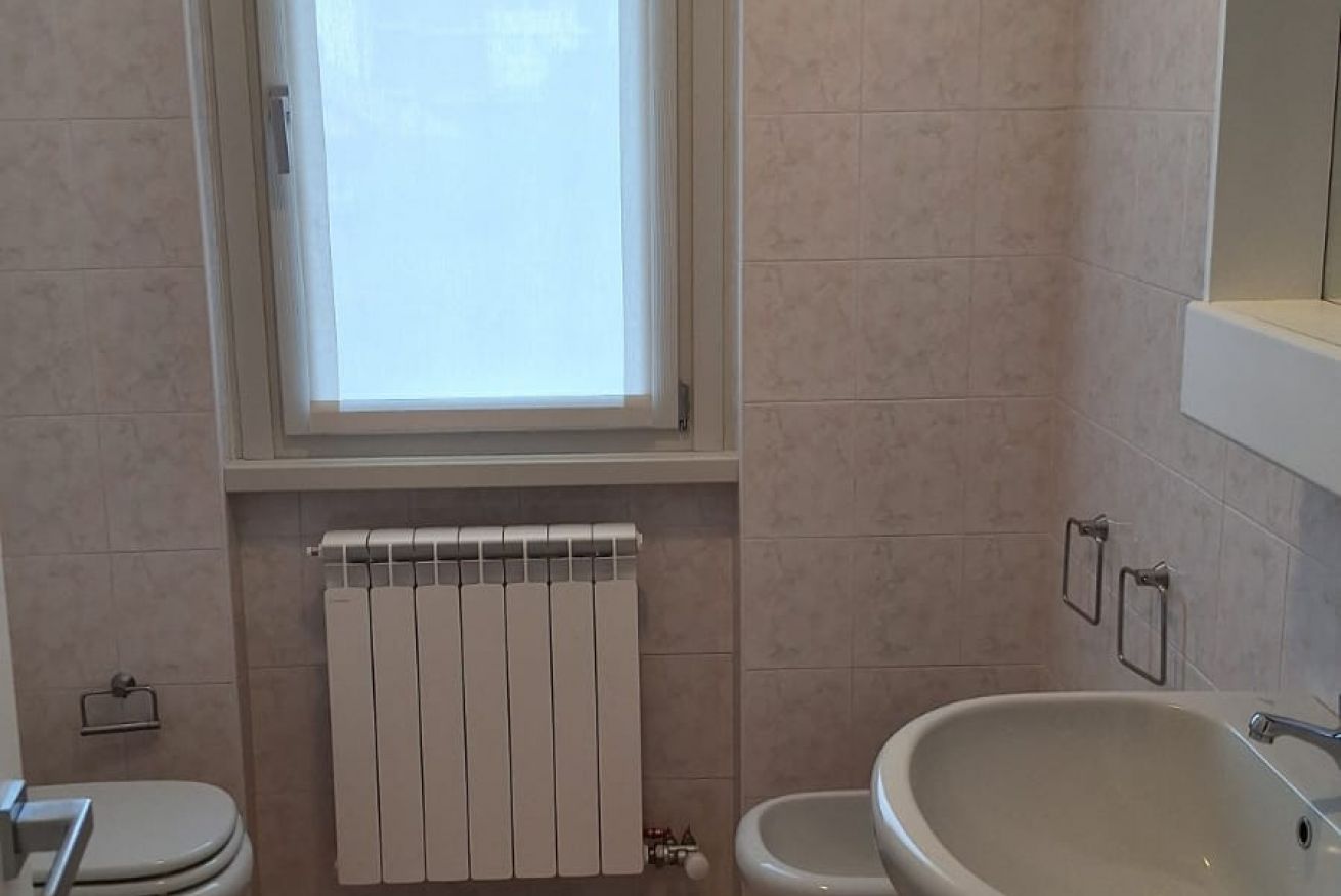 Une salle de bain comprenant des toilettes, un bidet, un lavabo, une fenêtre et un radiateur.