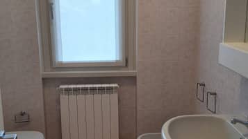 Une salle de bain comprenant des toilettes, un bidet, un lavabo, une fenêtre et un radiateur.