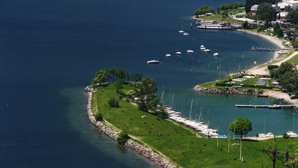 An aerial view of a coastal marina with boats docked along the shore, surrounded by greenery and residential buildings. - Terraced villa Golden Lake 1 - a few steps from the lake (Dervio)