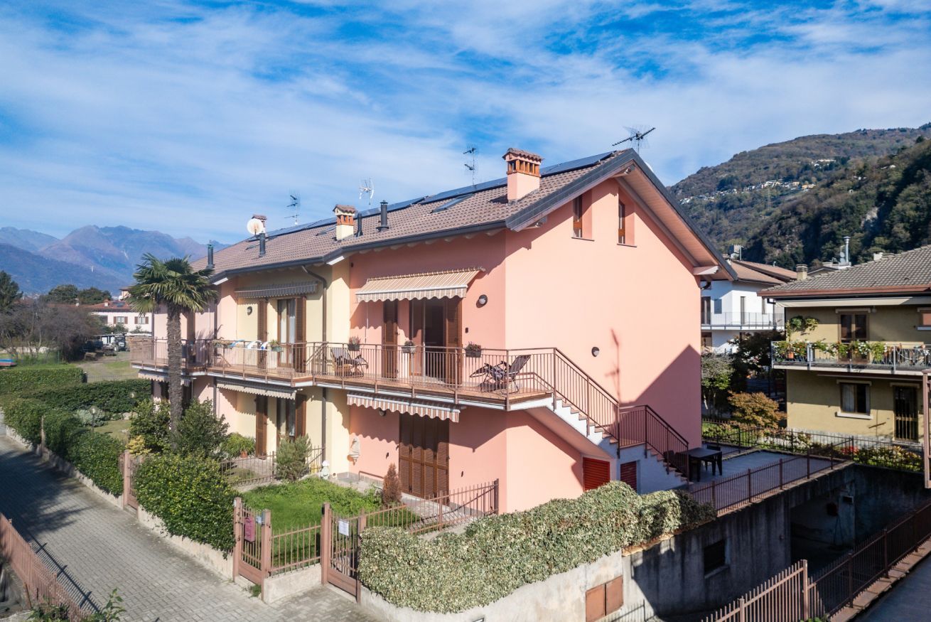 Une maison à deux étages avec un balcon, un petit jardin et une vue sur les montagnes en arrière-plan.