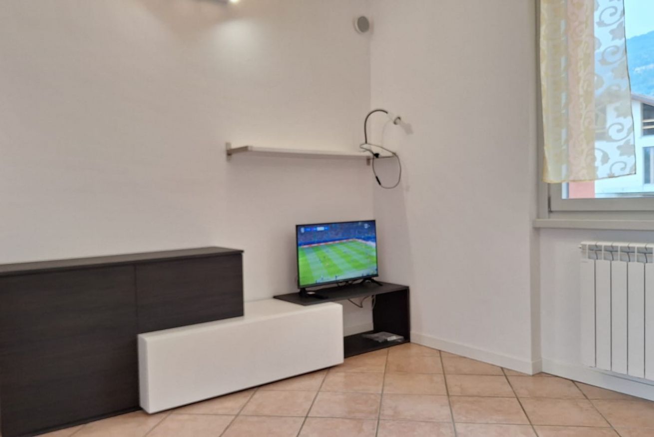 Ein modernes Wohnzimmer mit einem Flachbildfernseher auf einem schwarzen Standfuß, einem weißen Sofa und einer Heizung an der Wand.