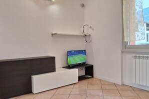 Ein modernes Wohnzimmer mit einem Flachbildfernseher auf einem schwarzen Standfuß, einem weißen Sofa und einer Heizung an der Wand.
