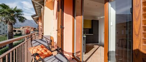 A balcony with a sun lounger, a glass door leading to a kitchen, and a view of mountains.