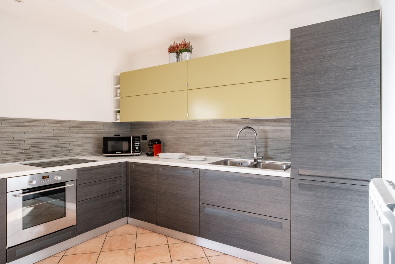 A modern kitchen with grey cabinets, a yellow upper shelf, a built-in oven, a microwave, and a sink.