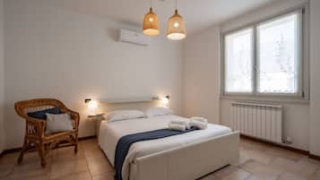 Une chambre à coucher avec un lit, un fauteuil en osier, des lampes de chevet et une fenêtre donnant sur un beau paysage.