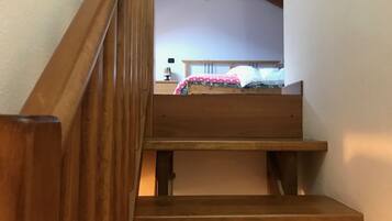 Eine Holztreppe führt zu einem Schlafzimmer mit einem Bett, einem Nachttisch und einer Lampe.