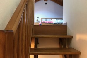 Una escalera de madera que conduce a un dormitorio con cama, mesita de noche y lámpara.