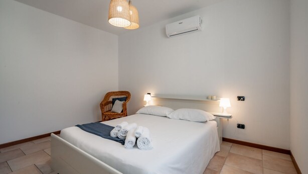 Un dormitorio ordenado con una cama, una silla y una mesita de noche con una lámpara.