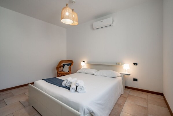 Un dormitorio ordenado con una cama, una silla y una mesita de noche con una lámpara.