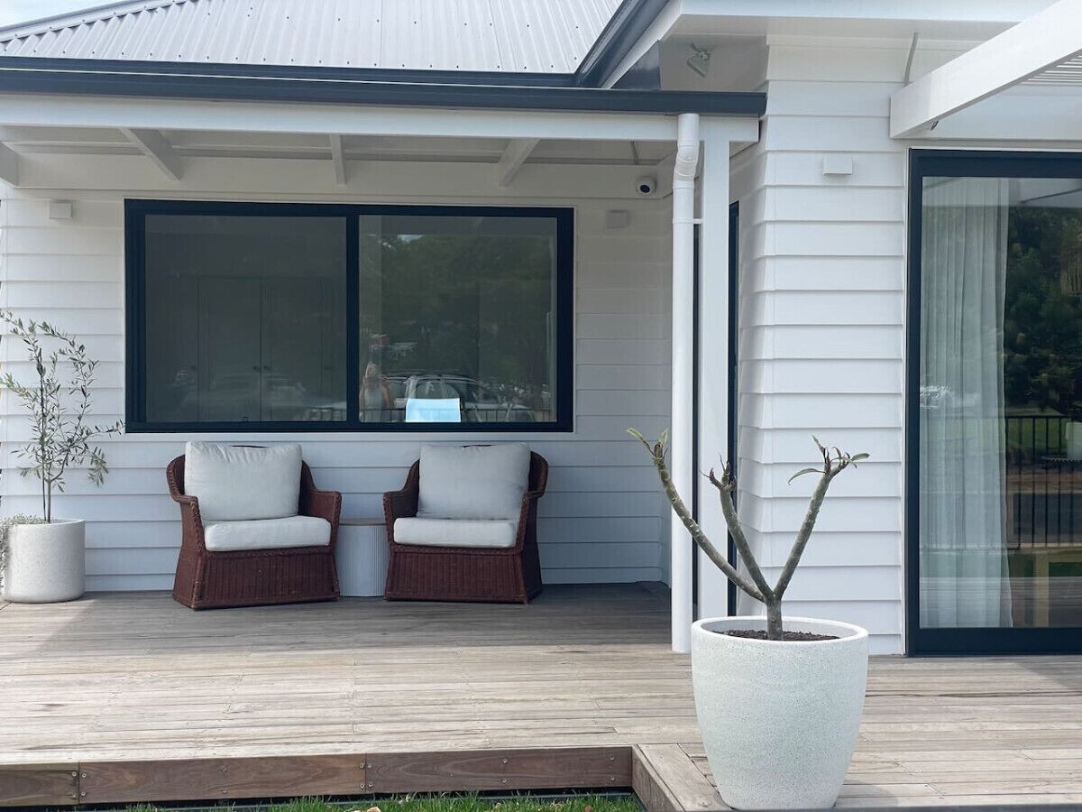 Een modern huis met een overdekte veranda, twee rieten stoelen en een bloempot.