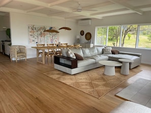 Una sala moderna con un sofá seccional, una mesa de comedor con sillas y un amplio ventanal con vistas al exterior.