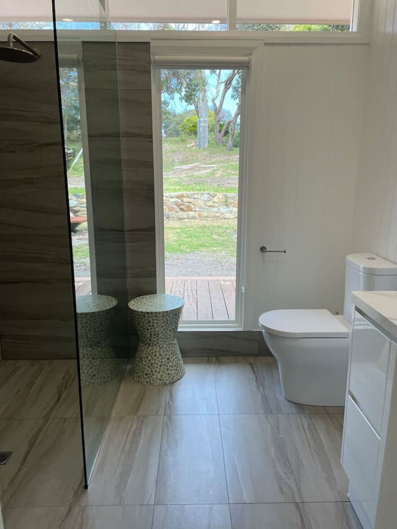 Une salle de bain moderne équipée d’une douche, de toilettes et de deux petites tables rondes.