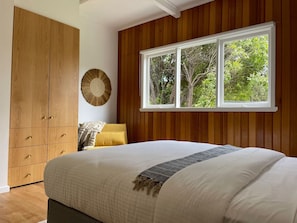 Un dormitorio con una cama grande, un armario de madera y una ventana con vista a árboles.