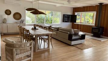Amplia sala de estar con piso de madera, una mesa de comedor con sillas, un sofá y un televisor.