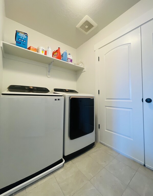 A laundry room with two stacked washers and dryers, a shelf with cleaning supplies, and a white door.