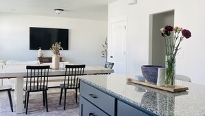 A modern kitchen with dark cabinets, a granite countertop, and a dining area with a table and chairs. - Hot Tub - Cozy Retreat in Springville (Springville)