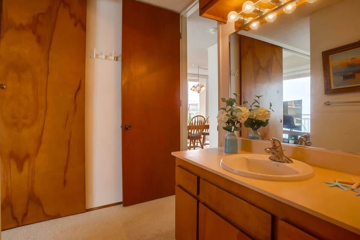 A bathroom with a wooden door, a sink with a mirror, and a vase with flowers.