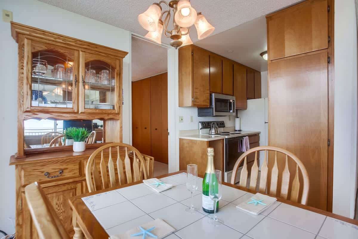 Un coin repas avec une table dressée pour deux personnes, une bouteille de champagne et un buffet contenant de la verrerie.