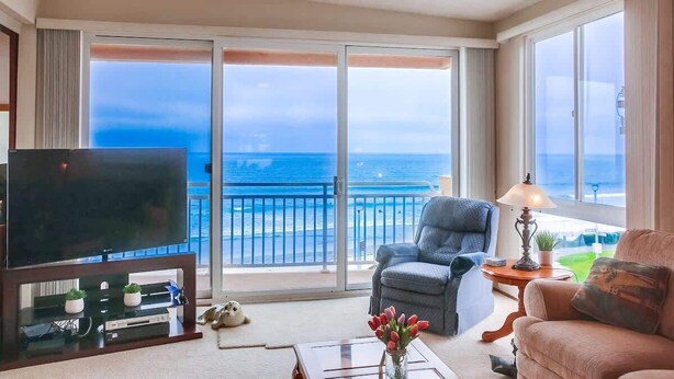 Ein Wohnzimmer mit Fernseher, einer Couch, einem Sessel und einem Balkon mit Meerblick.