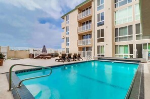 Une piscine avec des chaises longues et un bâtiment doté de balcons.