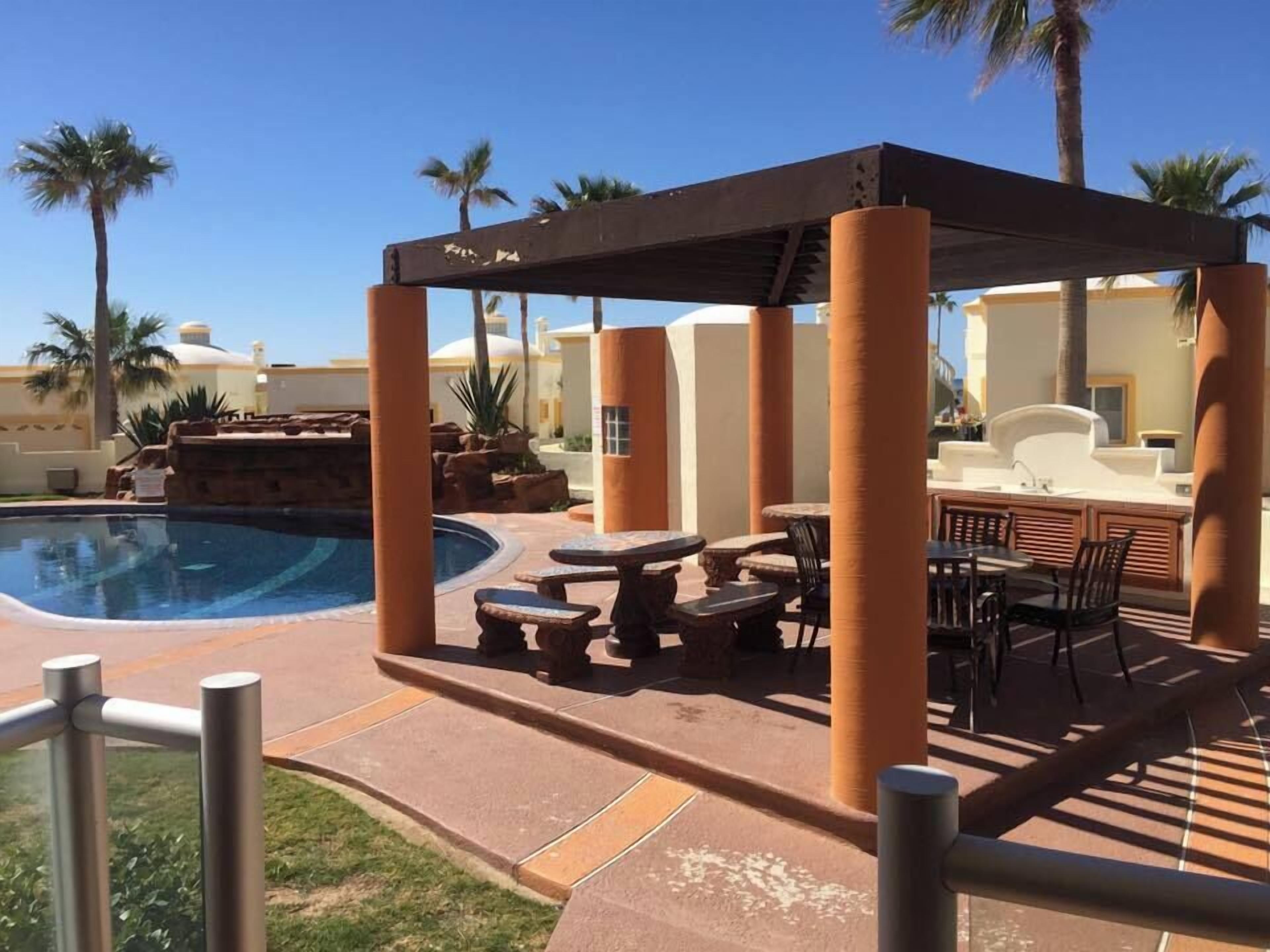Ein Poolbereich mit überdachter Sitzgelegenheit, einem Pool und Palmen.