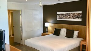 A hotel room with a large bed, a ceiling fan, a bedside lamp, and a painting on the wall. - 180˚ Water View Apartment - Simply Stunning (Urangan)