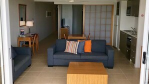 A modern living room with a sofa, coffee table, and a dining area with a table and chairs. - 180˚ Water View Apartment - Simply Stunning (Urangan)