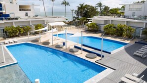 A rooftop pool with clear blue water, surrounded by lounge chairs and palm trees, overlooking a beach. - 180˚ Water View Apartment - Simply Stunning (Urangan)