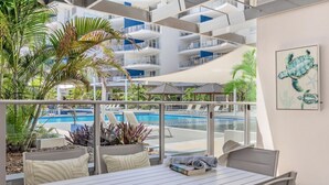 Un balcon avec vue sur la piscine, des sièges d’extérieur et une œuvre d’art représentant une tortue.
