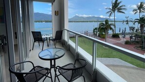 A balcony with a glass table and chairs, overlooking a body of water and palm trees.
