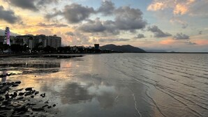 A beach with a calm sea, a rocky shoreline, and buildings in the background.