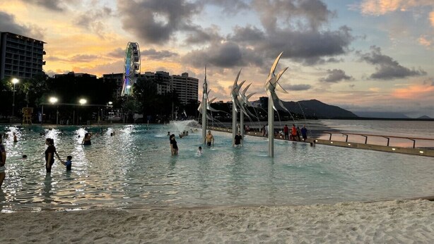A public swimming area with people enjoying the water, surrounded by buildings and a sunset sky.