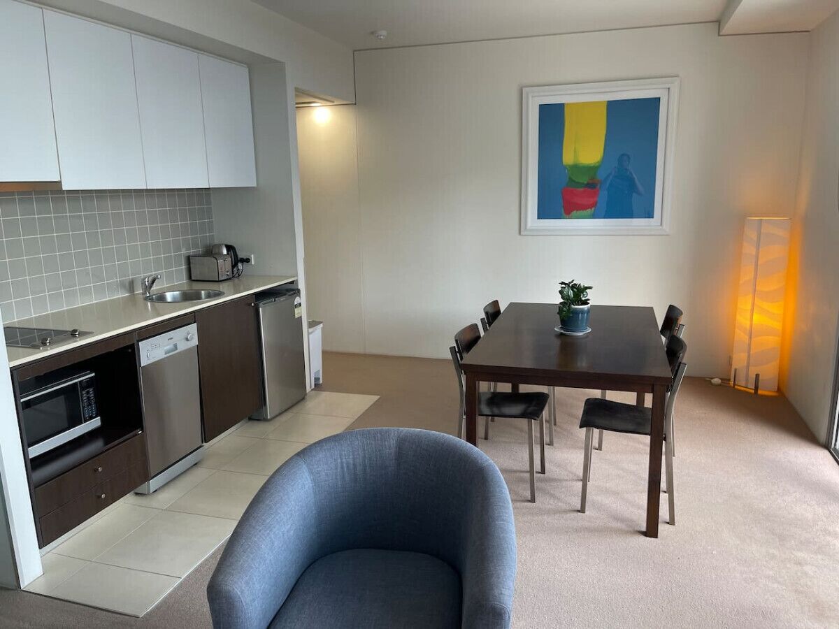 A modern kitchen with white cabinets, a dining table with chairs, and a blue armchair.