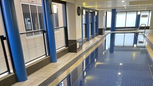 A long, narrow indoor pool with blue tiled floors and walls, surrounded by blue pillars and a tiled wall with windows. - Amazing City Skyline Apartment - Pool, Gym, Sauna. (Adelaide)