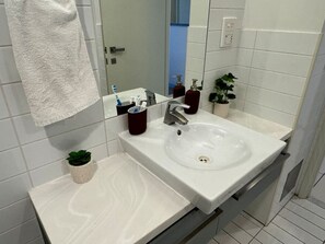Un baño con un lavamanos blanco, un espejo, un perchero para toallas y una pequeña planta en maceta.